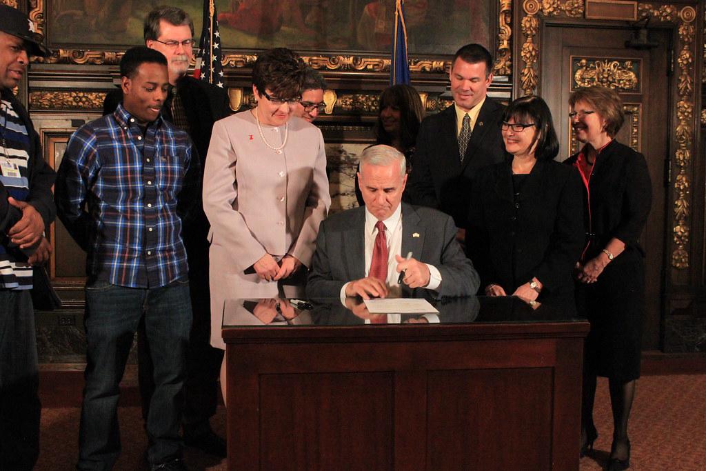 A state governor signing an executive order, surrounded by state officials